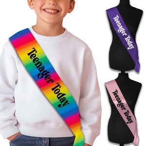 May include: A person wears a rainbow sash printed with "Teenager Today" in black. Two other sashes are shown, one purple and one pink, each with the same text, displayed on mannequins.