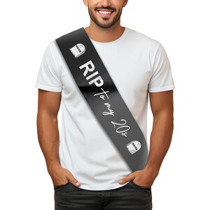 May include: Black satin sash with white text that reads "RIP to my 20s". The sash has two small white tombstone graphics with the word "youth" on them.