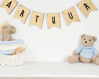 May include: A wooden banner spelling "ARTHUR" hangs above a white surface. A stuffed dinosaur and a basket with a brush and folded towels are on the left. A teddy bear wearing a blue sweater sits on the right. The scene is set against a white background.