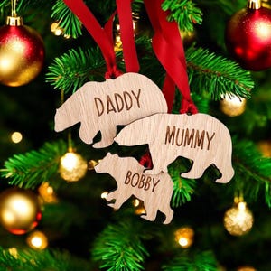 May include: Three wooden bear ornaments with red ribbon hangers. The bears are decorated with the names "Daddy", "Mummy", and "Bobby".
