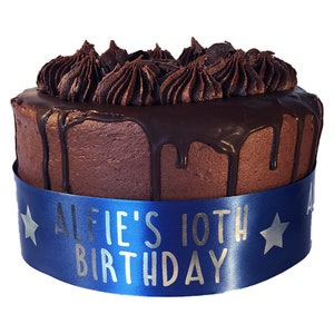 May include: A chocolate cake with chocolate frosting and a blue ribbon that says "Alfie's 10th Birthday" in silver lettering.