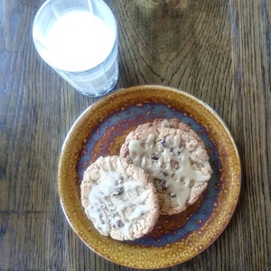 May include: Overhead shot of a glass of milk and two cookies on a plate. The cookies are round, with a light brown color and a drizzle of icing. The plate is brown and blue. The glass is clear and the milk is white.