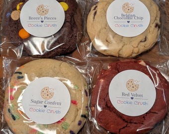 May include: Four individually wrapped cookies on a wooden surface. The cookies are labeled "Reece's Pieces", "Belgian Chocolate Chip", "Sugar Confetti", and "Red Velvet" with the "Cookie Crush" logo. The cookies are various colors and textures.