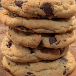May include: A stack of five golden-brown chocolate chip cookies. Each cookie is thick and has large, dark chocolate chunks throughout. The cookies are stacked on top of each other, creating a tempting treat.