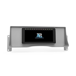 May include: A gray dashboard component with a rectangular screen displaying a logo and website address. The screen is surrounded by a black bezel and has a row of colored lights above it. The component has mounting tabs on each side.