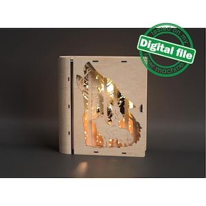 Peut inclure: Une découpe en bois d'un loup hurlant à la lune avec une femme à dos. La découpe est éclairée par derrière, créant une lueur chaude. Les mots "Fichier numérique" sont imprimés sur un cercle vert dans le coin supérieur droit de l'image.