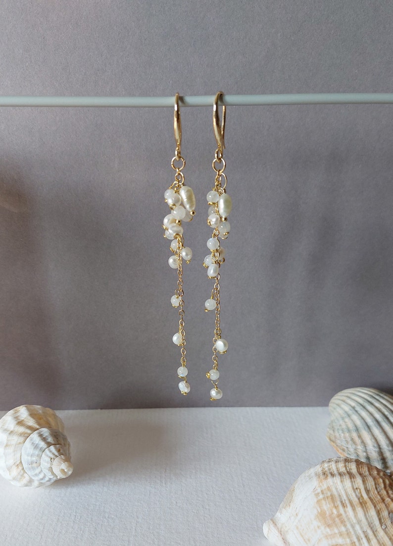 May include: Elegant gold-tone earrings with cascading white pearls. The earrings feature a cluster of pearls at the top, with delicate chains of smaller pearls dangling below. The design is simple yet sophisticated, perfect for special occasions.
