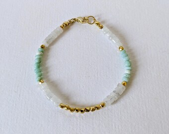 May include: A delicate bracelet featuring a combination of white, light green, and gold beads. The bracelet is strung together with a gold clasp and gold accent beads. The beads are small and round, creating a subtle and elegant accessory.