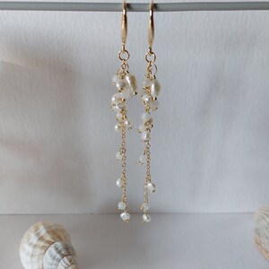 May include: Elegant gold-tone earrings with cascading white pearls. The earrings feature a cluster of pearls at the top, with delicate chains and smaller pearls extending downwards. The design is simple yet sophisticated, perfect for special occasions.