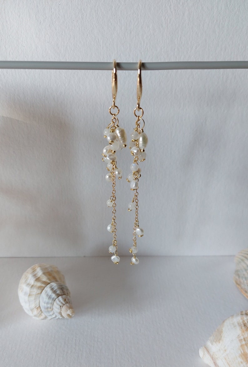 May include: Elegant gold-tone earrings with cascading white pearls. The earrings feature a cluster of pearls at the top, with delicate chains and smaller pearls extending downwards. The design is simple yet sophisticated, perfect for special occasions.