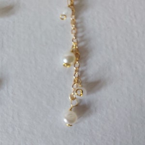 May include: A delicate gold chain adorned with clusters of small, creamy white pearls. The chain cascades downward, with larger pearls suspended at intervals. The pearls have a subtle luster, creating an elegant and timeless aesthetic.