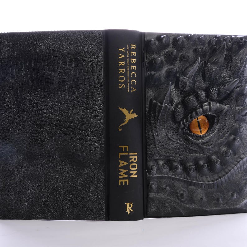 May include: A black leather-bound book with a dragon embossed on the cover. The spine reads "Iron Flame" by "Rebecca Yarros".