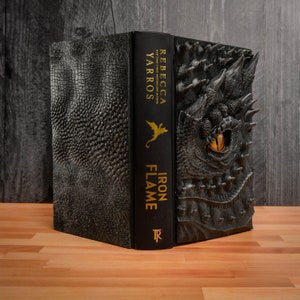 May include: A black hardcover book with a dragon embossed on the cover. The title "Iron Flame" and the author "Rebecca Yarros" are printed in gold on the spine.