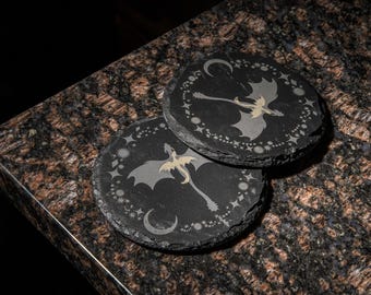 May include: Two black slate coasters with a gold dragon silhouette design and a crescent moon and stars pattern.