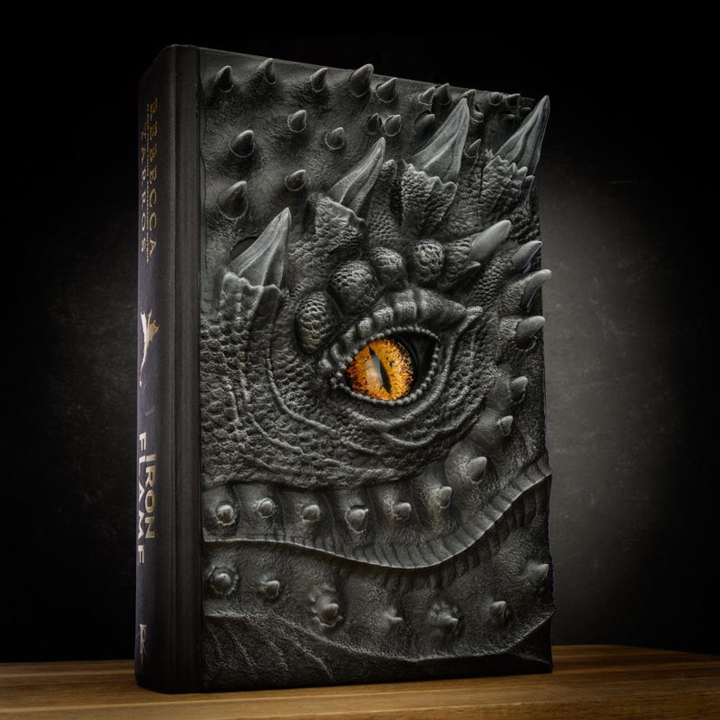 May include: A black leather-bound book with a dragon's head embossed on the cover. The dragon's eye is a bright orange color.