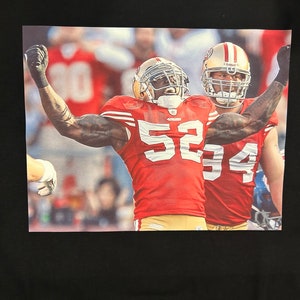 May include: Two football players wearing red and gold uniforms with the number "52" and "94" on their jerseys. The players are celebrating a touchdown with their arms raised in the air. The background is a blurred image of a crowd of people.