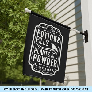 May include: A black rectangular garden flag featuring white text that reads EST. 1789 POTIONS PILLS PLANTS & POWDER SALEM, MA. The design includes a graphic of a bird perched on a line, all enclosed within a decorative white border frame.