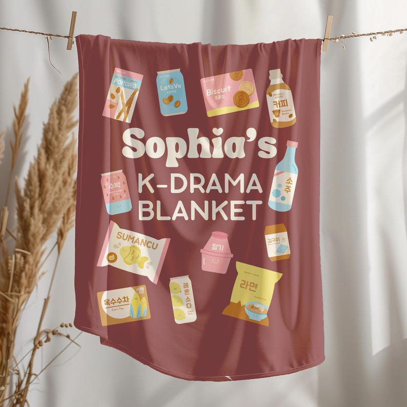 May include: A maroon K-Drama blanket with various food and drink illustrations, including snacks, drinks, and a bottle of soju. The blanket has the text "Sophia's K-DRAMA BLANKET" in white, making it a fun gift for fans of Korean dramas.