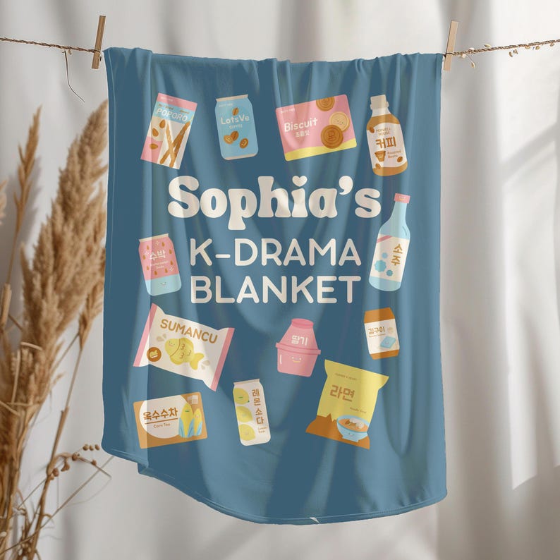May include: A blue blanket with the text "Sophia's K-DRAMA BLANKET" and various food and drink illustrations. The blanket features images of snacks, drinks, and Korean text.