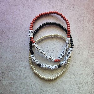 May include: Three beaded bracelets. One is red, one is black, and one is silver. The black and red bracelets have white letter beads spelling "MY CHEMICAL ROMANCE" and "THE BLACK PARADE".