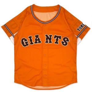 Puede incluir: Camiseta de béisbol naranja con ribetes negros y blancos. La camiseta tiene "GIANTS" escrito en letras marrones en el pecho y "YOMI" escrito en las mangas.