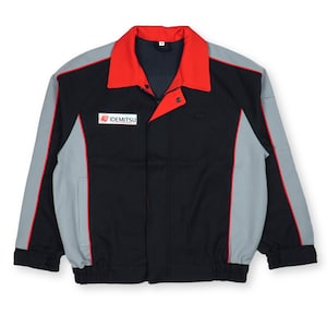 May include: A black, gray, and red work jacket with the "IDEMITSU" logo on the chest. The jacket has a red collar and red trim along the gray sleeves. The jacket has a button closure and two front pockets.