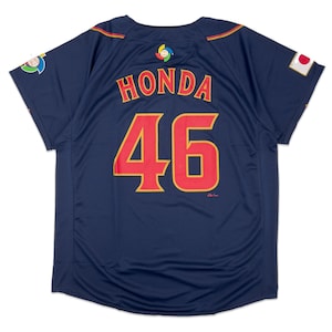 Puede incluir: Una camiseta de béisbol azul marino con letras rojas y doradas. La camiseta tiene el nombre "HONDA" y el número "46" en la espalda.