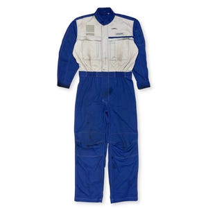 May include: A blue and white jumpsuit with a white patch on the chest that says "REBELION". The jumpsuit has a zipper and a collar.