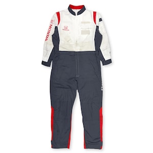 May include: A white, navy blue, and red Honda racing jumpsuit. The jumpsuit features the Honda logo on the chest and sleeve, with red accents on the collar, shoulders, and legs. The jumpsuit has a zip-up front and long sleeves.