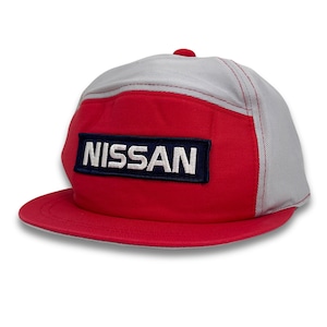 Puede incluir: Una gorra de béisbol roja y gris con un logotipo "NISSAN" blanco en un rectángulo azul marino.