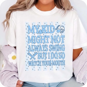 Op de afbeelding: Wit T-shirt met een lichtblauw honkbalontwerp. De tekst luidt "MY KID MIGHT NOT ALWAYS SWING BUT I DO SO WATCH YOUR MOUTH" in een speels lettertype, met honkbalknuppels en een helm.