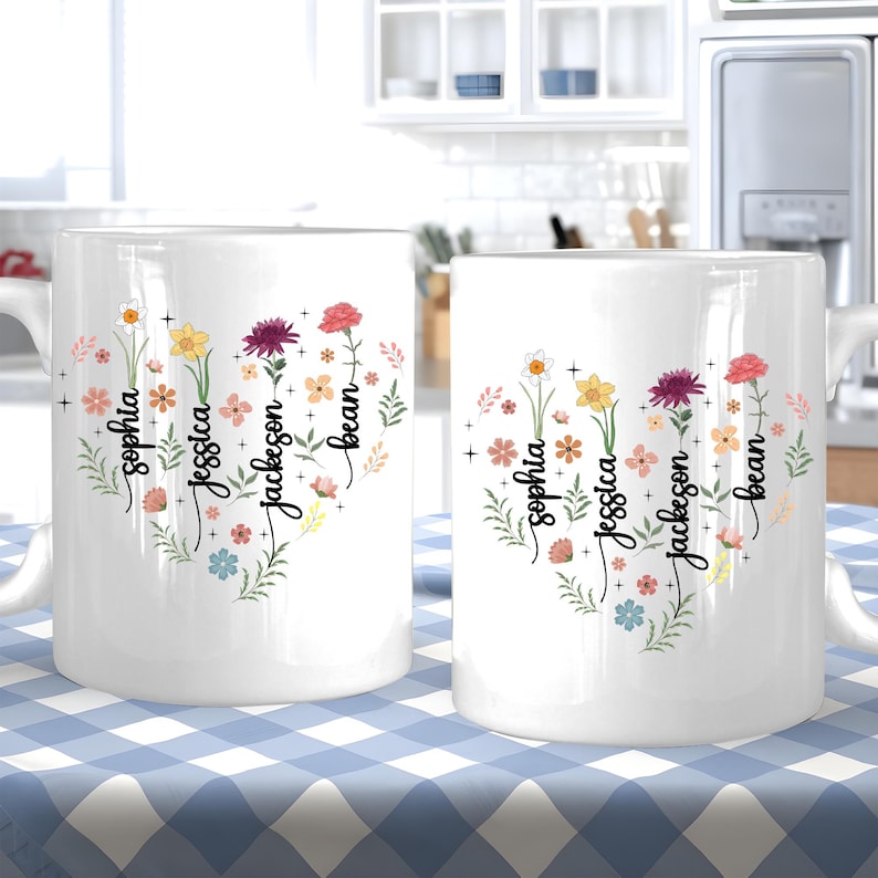 May include: Two white ceramic mugs with floral designs and names "Sophia", "Jessica", "Jackson", and "Bean" written on them. The mugs are on a blue and white checkered tablecloth.
