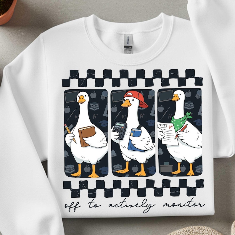 Peut inclure: Sweat-shirt blanc avec un motif fantaisiste de trois oies dans un cadre scolaire. Chaque oie est repr&eacute;sent&eacute;e avec des fournitures scolaires, dont un livre, une calculatrice et une feuille de test. Le texte "off to actively monitor" est en bas.