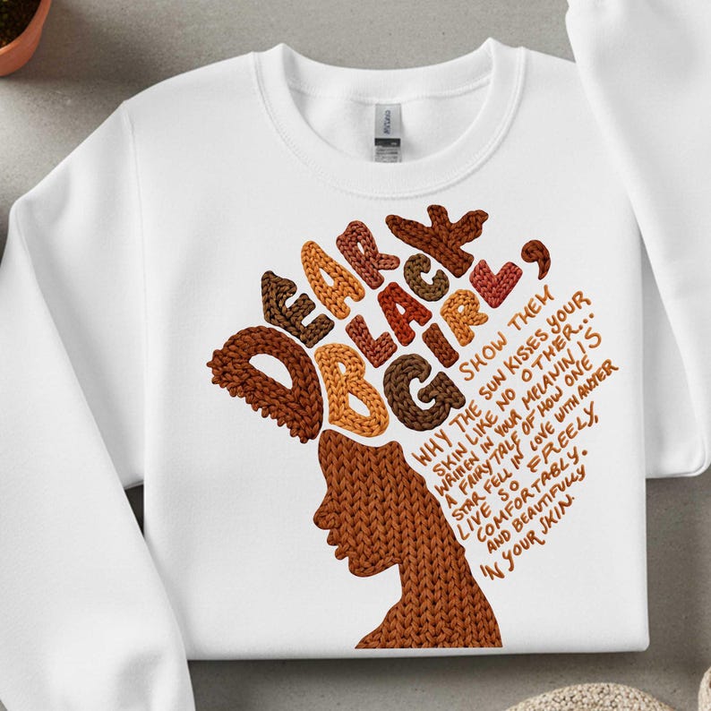 May include: White sweatshirt with the text "Dear Black Girl" in brown and orange lettering. The design includes a silhouette of a woman with a knitted hair design and additional text that reads "Why the sun kisses your skin..."