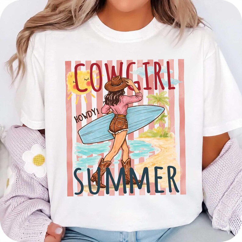 Może przedstawiać: Biała koszulka z grafiką przedstawiającą kowbojkę trzymającą deskę surfingową na plaży. Projekt zawiera słowa "COWGIRL SUMMER" i "HOWDY!" w zabawnej czcionce, ze słońcem i palmami.