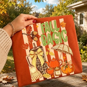 May include: A rust-coloured graphic featuring the words "FALL BASIC" in green, with autumn-themed illustrations. The design includes a coffee tumbler, teapot, pumpkin, and leaves, set against striped background.