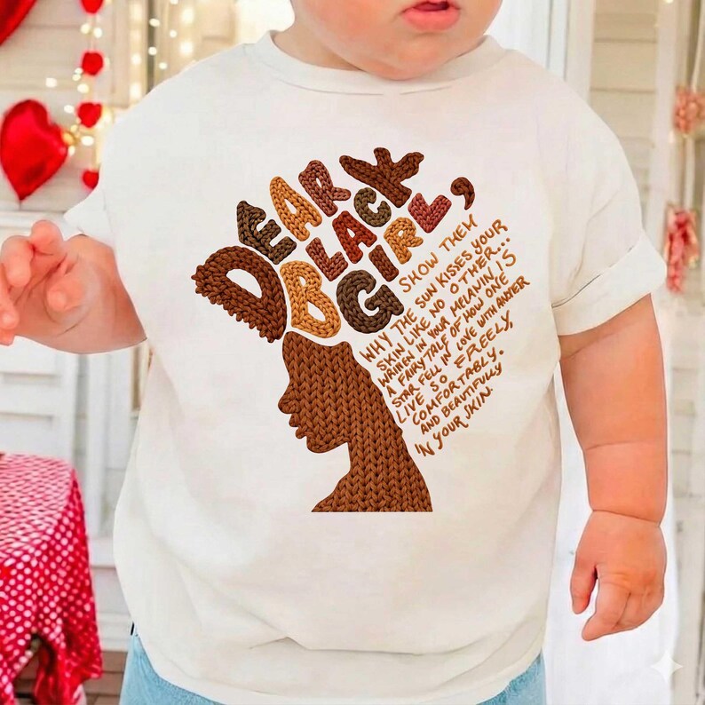 May include: A white t-shirt featuring the text "DEAR BLACK GIRL" in brown and tan letters, with a silhouette of a woman's face in brown. The shirt also includes a poem about melanin and self-love.