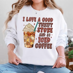 May include: White sweatshirt with the text "I LOVE A GOOD THRIFT STORE AND £8 ICED COFFEE" in brown lettering. The graphic features an iced coffee with whipped cream and a patchwork sleeve.