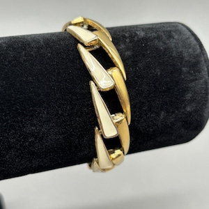 May include: A gold-tone bracelet with a bold, chain-link design. The links alternate between solid gold and cream-colored enamel, creating a striking contrast. The bracelet is displayed on a black velvet surface.