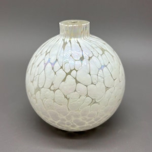 May include: A round, white glass vase with a textured, bubble-like pattern. The vase has a short neck and a pearlescent sheen, reflecting hints of blue and purple. The overall design is organic and decorative.