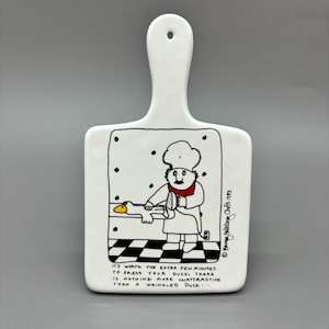 May include: White ceramic chopping board with a cartoon chef ironing a duck. The text reads: "It's worth the extra few minutes to press your duck. There is nothing more unattractive than a wrinkled duck..."