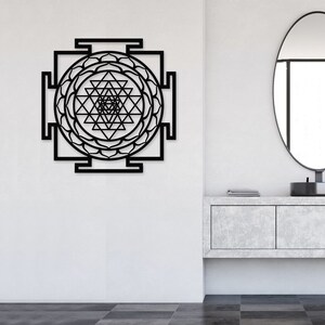 Puede incluir: Arte de pared de metal negro con un dise&ntilde;o geom&eacute;trico y un mandala circular en el centro. El dise&ntilde;o recuerda a un Sri Yantra, un s&iacute;mbolo sagrado en el hinduismo.