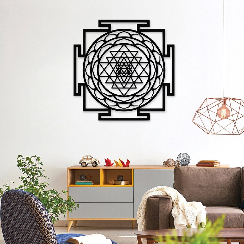 Puede incluir: Arte de pared de metal negro con un dise&ntilde;o geom&eacute;trico de un Sri Yantra, un s&iacute;mbolo sagrado en el hinduismo. El arte se muestra en una pared blanca en un ambiente de sala de estar.