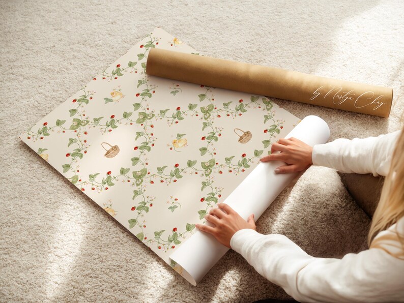 May include: Wallpaper roll with a repeating pattern of strawberries, leaves, and small baskets on a cream background. A brown paper tube rests on top. The text "by Marilyn Choy" is visible on the tube.