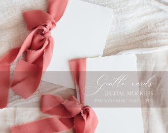May include: Two white cards with a frayed edge, tied with a coral ribbon bow. The cards are on a white linen background. The text on the image reads "Gentle cards DIGITAL MOCKUPS PSD WITH SMART OBJECT JPEG".