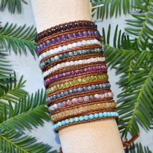 May include: A stack of colorful gemstone bracelets with leather wrappings. The bracelets feature various stones, including amethyst, turquoise, and rose quartz.