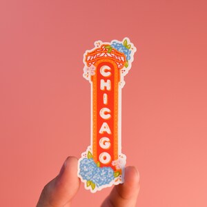 May include: A white sticker with a red and orange illustration of a Chicago sign with blue and white flowers on top. The sign says "CHICAGO" in white letters.