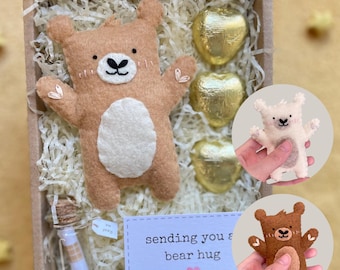 May include: A gift box filled with brown shredded paper, a small brown felt bear, three gold foil-wrapped chocolate hearts, a small glass bottle with a cork stopper, and a card that reads "sending you a bear hug".