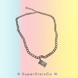 May include: Silver-toned chain necklace with a pendant shaped like a $100 bill. The necklace has a simple, yet bold design. The pendant features the number 100 and dollar signs. The necklace is displayed against a gradient background of pink, blue, and yellow.