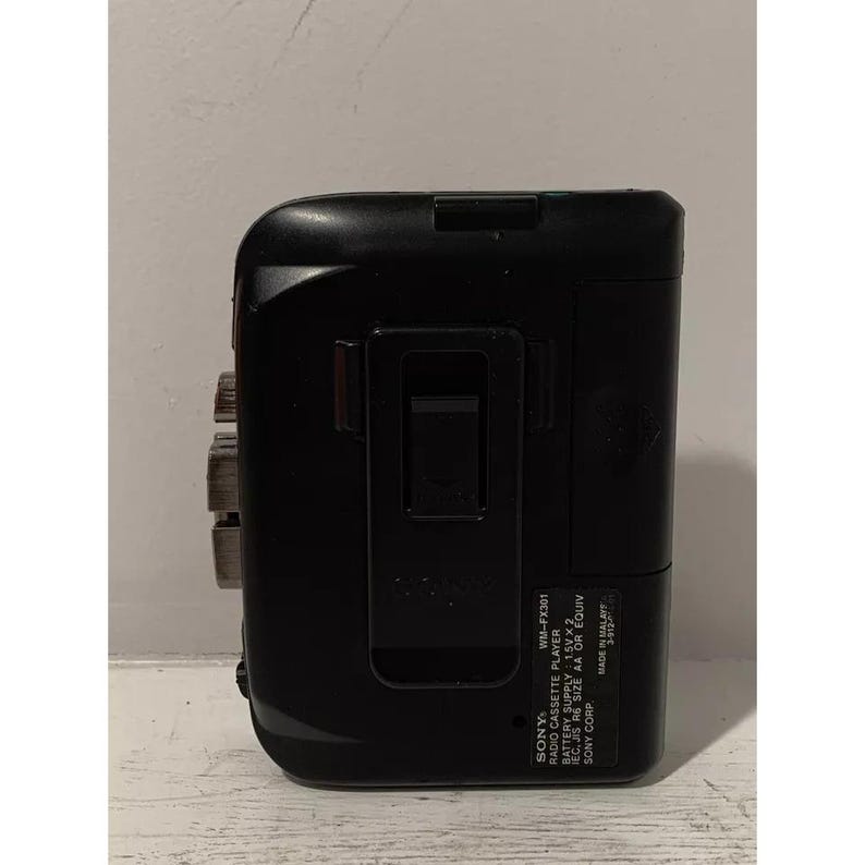 May include: Black Sony WM-FX301 radio cassette player with a silver face and a black belt clip. The text on the player reads "SONY WM-FX301 RADIO CASSETTE PLAYER BATTERY SUPPLY 1.5VX2 REC, JIS R6 SIZE AA OR EQUIV SONY CORP MADE IN MALAY"